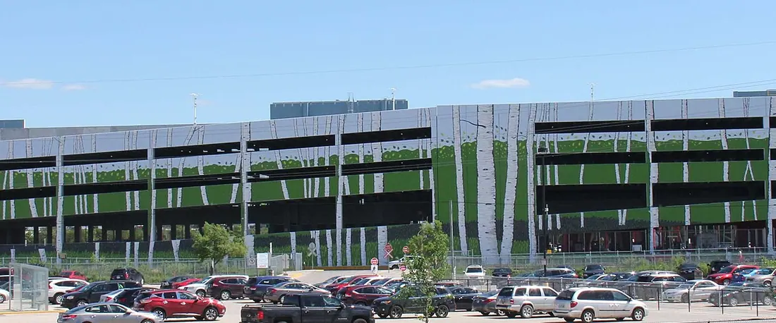Le côté nord du complexe du Club Regent Casino à Winnipeg : son garage de stationnement à plusieurs niveaux habillé d'une murale de bouleaux, au-dessus d'un stationnement plein