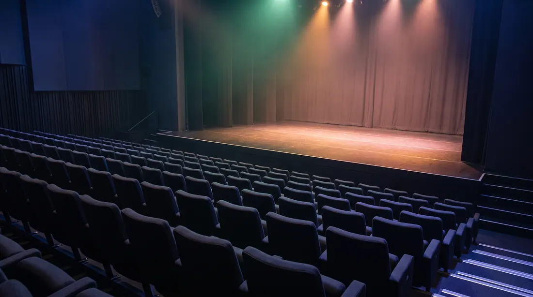 Une scène de spectacle vide sous un éclairage chaud, devant des rangées de sièges vides