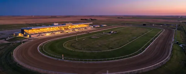 Une piste de course en terre vide et une tribune éclairée au crépuscule, vues d'en haut